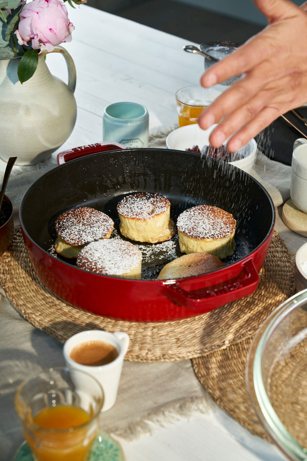 Roter Bräter mit Glasdeckel, gefüllt mit kleinen Kuchen, auf einem Tisch von oben fotografiert.