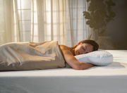 Frau schläft friedlich auf einem ergonomischen Schlafkissen in einem sanft beleuchteten Raum, Seitenansicht.