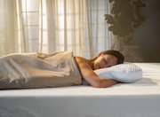 Frau schläft friedlich auf einem ergonomischen Schlafkissen in einem sanft beleuchteten Raum, Seitenansicht.