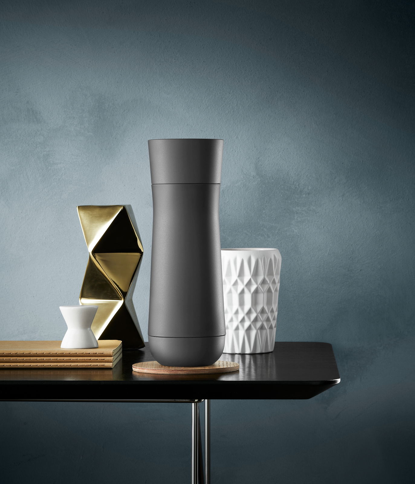 WMF isolierbecher 0,35l IMPULSE Schwarzer Impulse Isolierbecher 0,35l auf einem Tisch, umgeben von dekorativen Objekten, aus der Frontalperspektive.