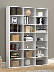 Weißes, modernes Regal mit 15 offenen Fächern, dekoriert mit Büchern, Vasen, Pflanzen und Boxen, in einem Wohnraum; Ansicht schräg von vorn.