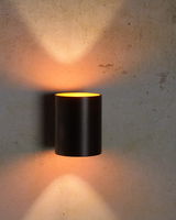 Moderne schwarze Wandleuchte XERA von Lucide mit zylindrischem Design, die warmes Licht nach oben und unten an die Wand strahlt. Frontalansicht.