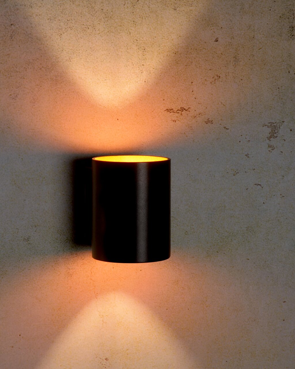 Moderne zwarte wandlamp XERA van Lucide met een cilindrisch ontwerp, die warm licht naar boven en naar beneden op de muur werpt. Vooraanzicht.