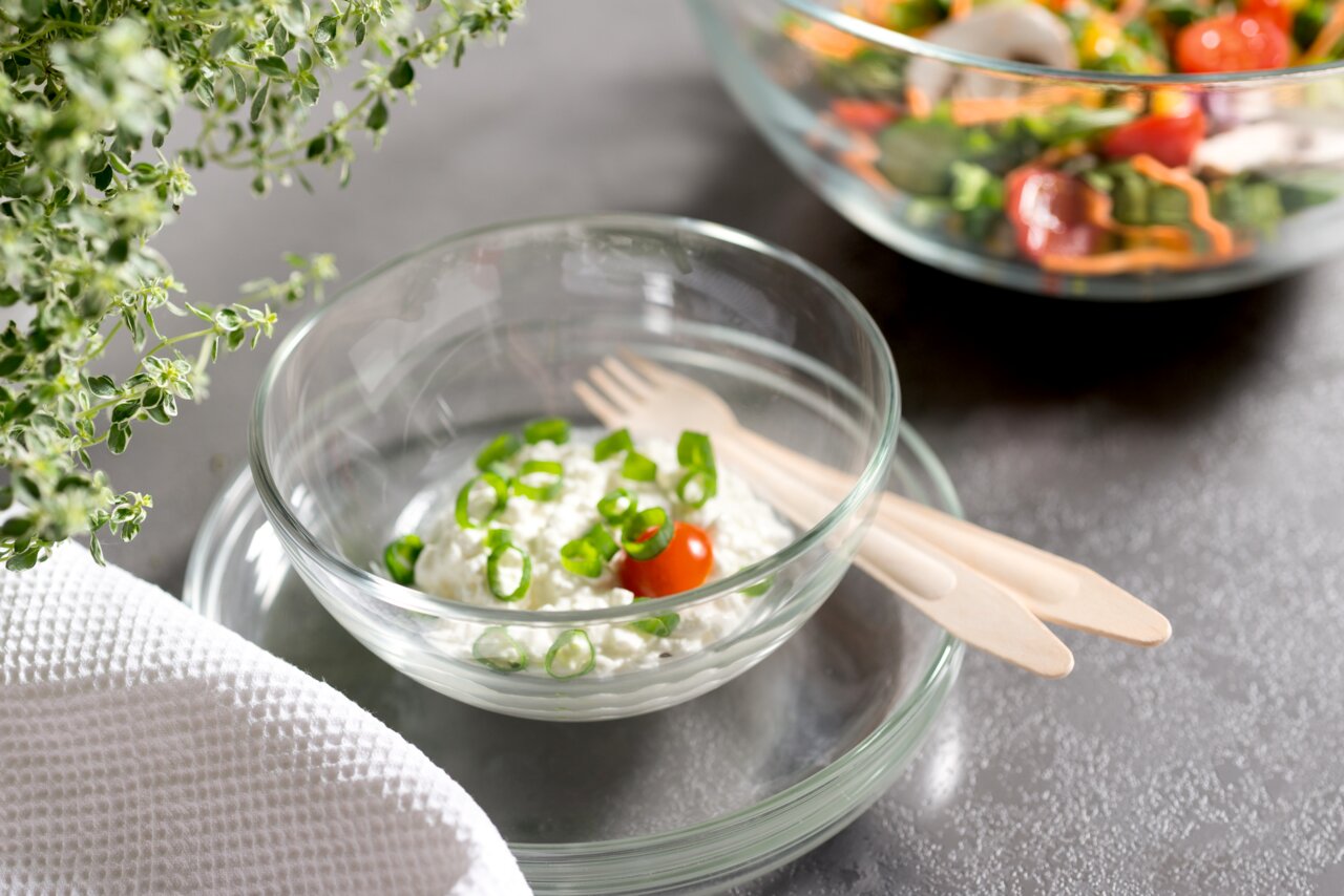 Glas-Schale Cucina 14cm mit Frischkäse, Frühlingszwiebeln und Kirschtomate, von oben fotografiert, neben Holzlöffeln und Kräutern.