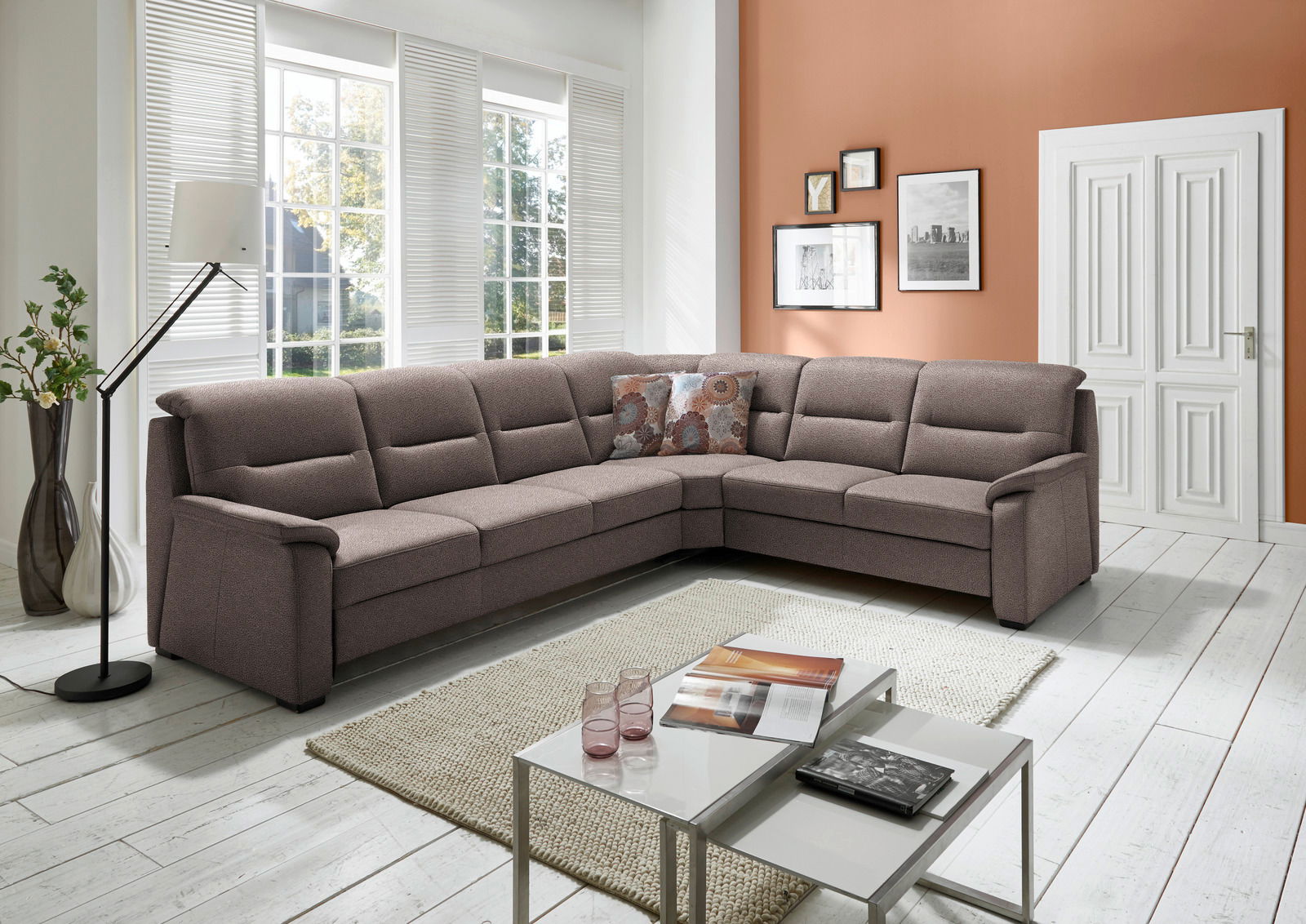 Beldomo Comfort Ecksofa ERFURT Große, moderne Polsterrundecke in einem hellen Wohnzimmer mit großen Fenstern, die viel Tageslicht hereinlassen. Die Couch ist in einem warmen Braunton gehalten und bietet viel Platz zum Entspannen. Perspektive von vorne links.