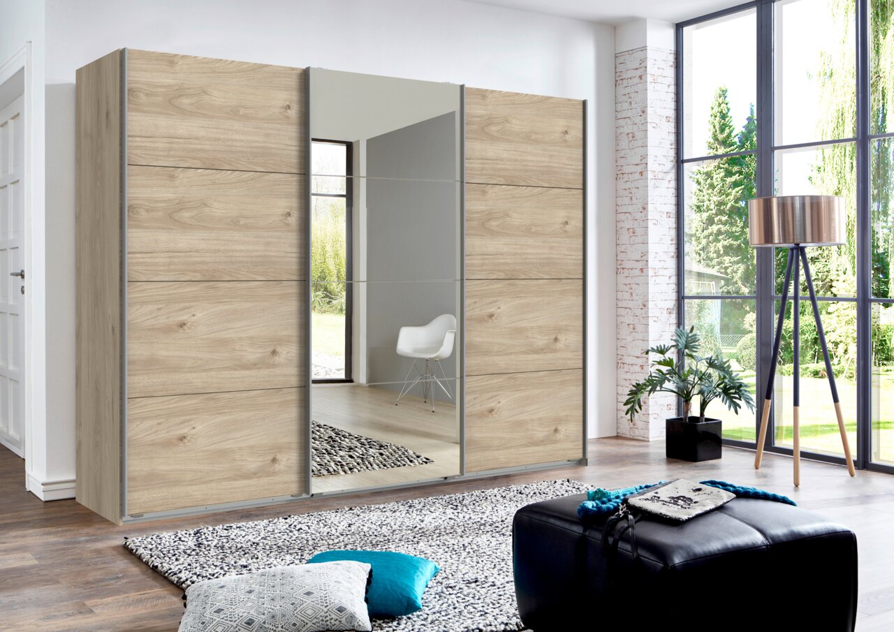 Moderner dreitüriger Schwebetürenschrank in Holzoptik mit Spiegeltür, seitliche Perspektive im hellen Wohnzimmer.