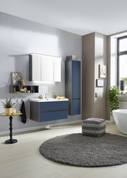 Moderne Badkombination in einer stilvollen Badezimmerumgebung, bestehend aus einem Waschtisch mit blauen Schubladen, einem Hängeschrank und einem Spiegelschrank, seitliche Perspektive.