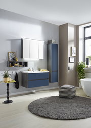 Moderne Badkombination in einer stilvollen Badezimmerumgebung, bestehend aus einem Waschtisch mit blauen Schubladen, einem Hängeschrank und einem Spiegelschrank, seitliche Perspektive.