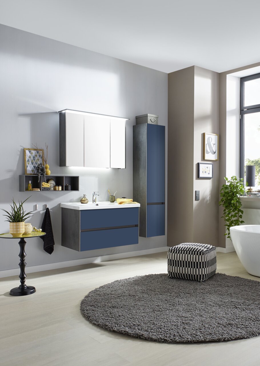 Moderne Badkombination in einer stilvollen Badezimmerumgebung, bestehend aus einem Waschtisch mit blauen Schubladen, einem Hängeschrank und einem Spiegelschrank, seitliche Perspektive.