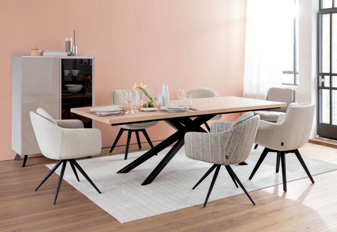 Moderner Esstisch mit hellem Holz und schwarzen Metallbeinen, umgeben von gepolsterten Stühlen in einem eleganten Esszimmer mit Blick auf die Tischplatte.