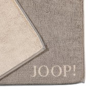 Grijze badmat met een beige rand en het opschrift 'JOOP!' in de hoek, gefotografeerd van bovenaf.