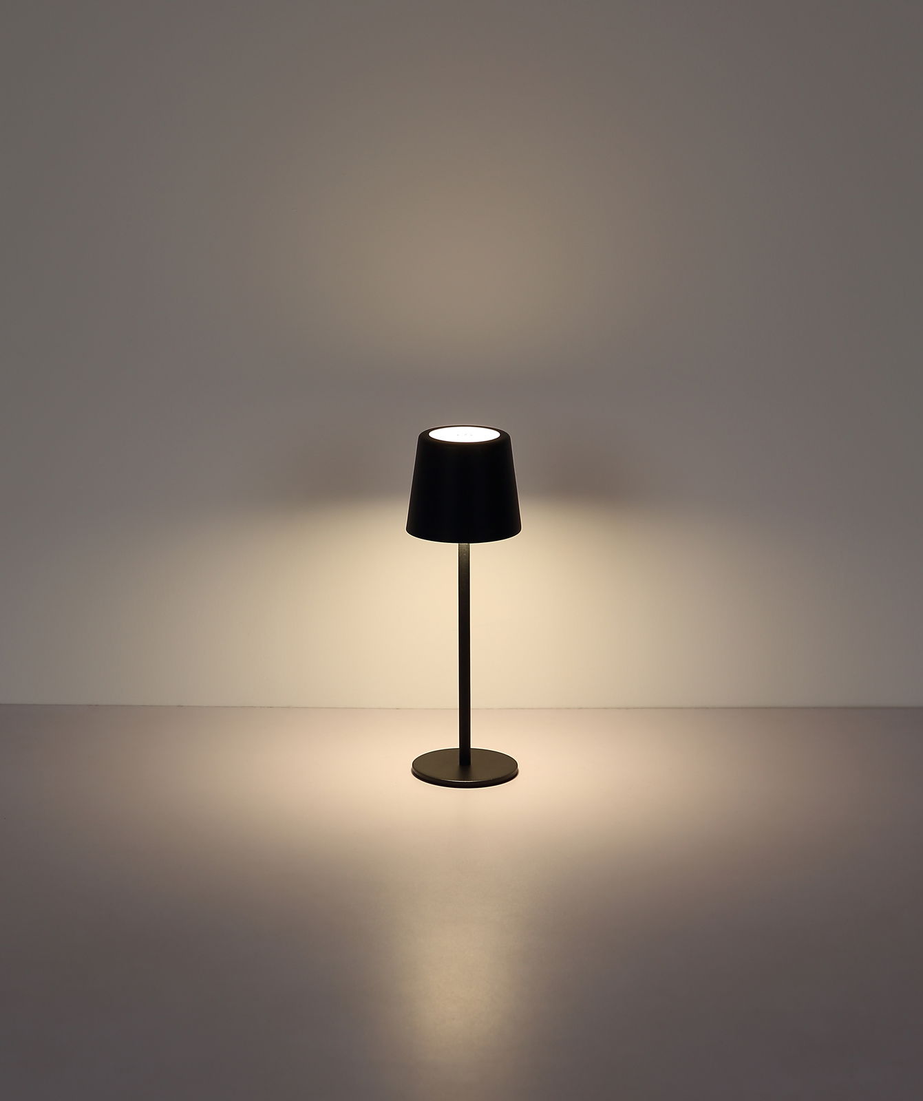 Moderne Tischleuchte in Schwarz, frontal fotografiert, mit sanftem Lichtschein auf einer glatten Oberfläche.