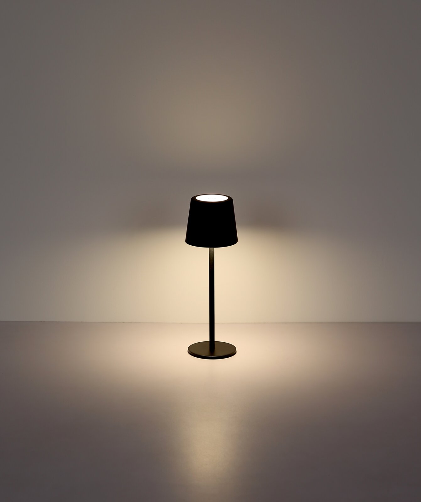 Moderne Tischleuchte in Schwarz, frontal fotografiert, mit sanftem Lichtschein auf einer glatten Oberfläche.