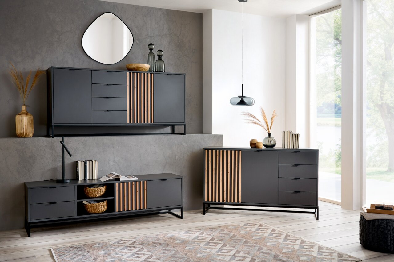 Voleo Sideboard PHIL Moderne Wohnzimmermöbel in dunklem Design mit Holzakzenten, bestehend aus einem Sideboard, einem XL-Sideboard und einem TV-Lowboard, aus der Perspektive eines hellen, geräumigen Raumes mit großen Fenstern.