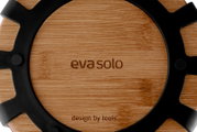 Close-up bovenaanzicht van een ronde houten Eva Solo onderzetter met zwart metalen frame en gegraveerd logo