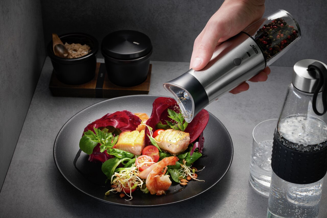 GEFU Salz-/Pfeffermühle VELO Hand hält eine Salz- und Pfeffermühle VELO über einem Teller mit frischem Salat und Lachs, seitliche Perspektive.