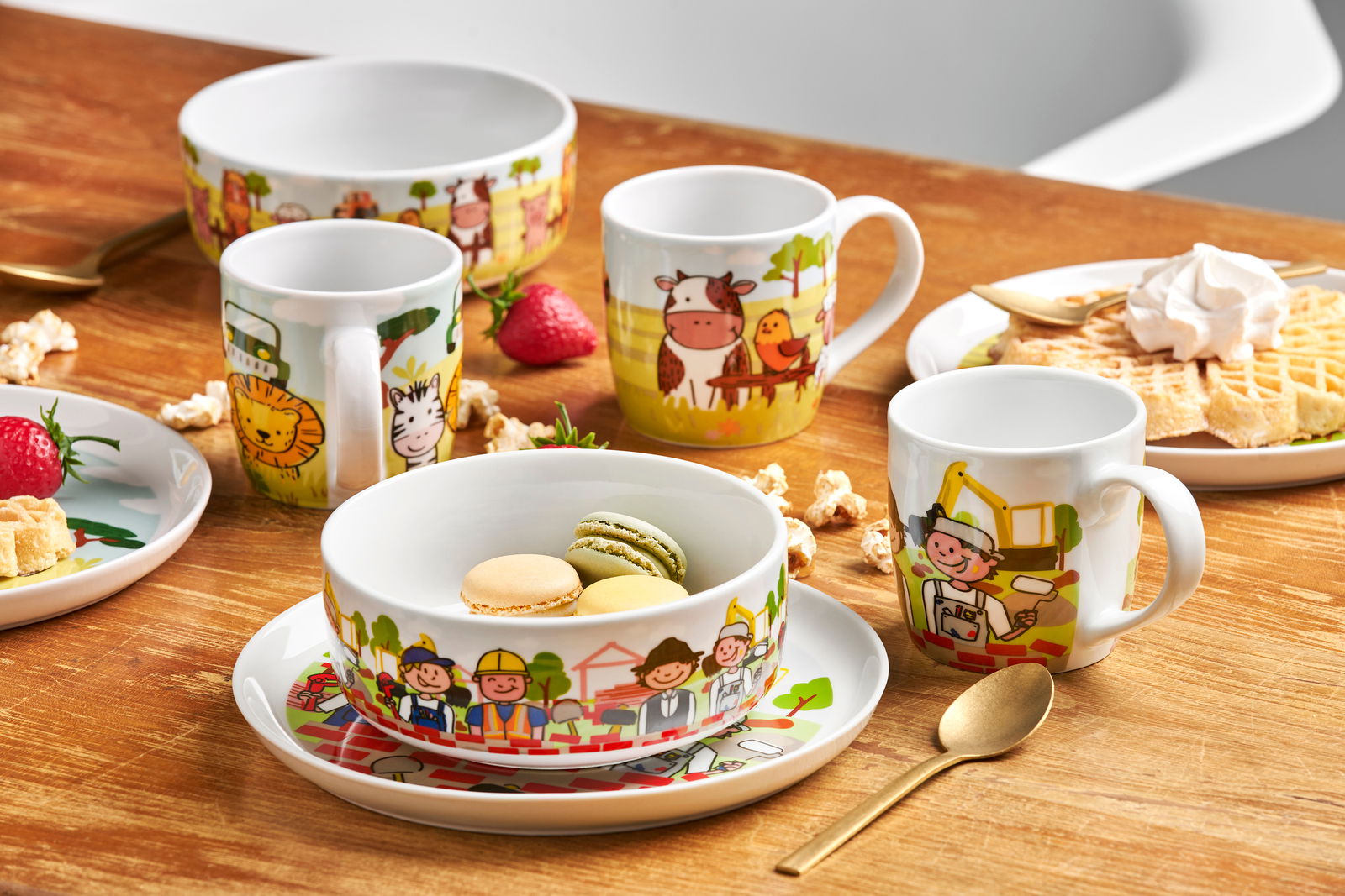 Kindergeschirr-Set mit Baustellenmotiven, bestehend aus Tasse, Schüssel und Teller, auf einem Holztisch arrangiert. Frontalansicht.