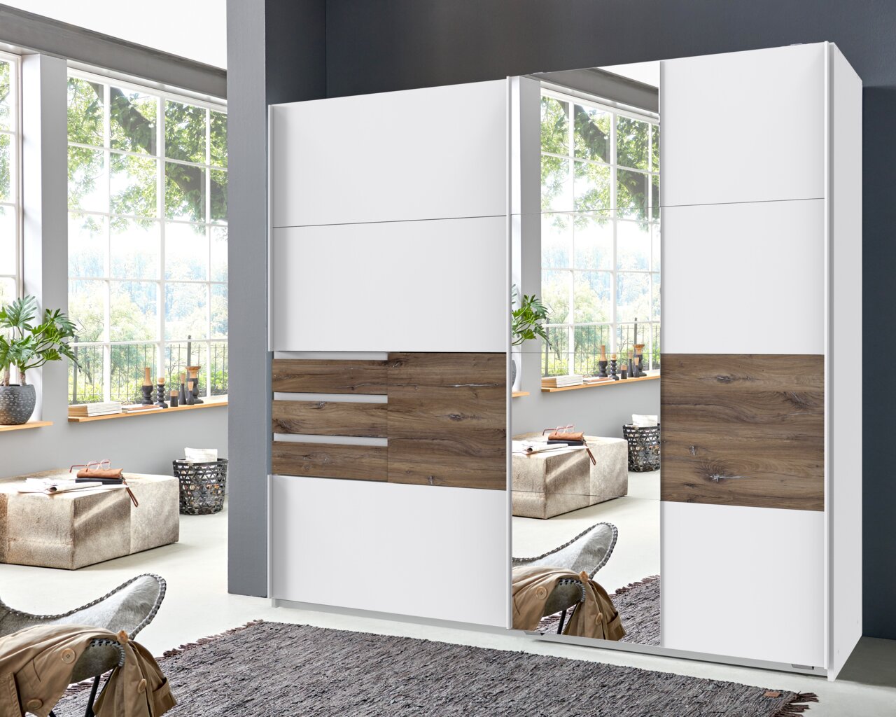 Z2 Schwebetürenschrank 2trg. BAMBERG Moderner Schwebetürenschrank mit zwei Türen, einer davon mit Spiegel, in einem hellen Raum mit großen Fenstern, aus der Frontalperspektive betrachtet.