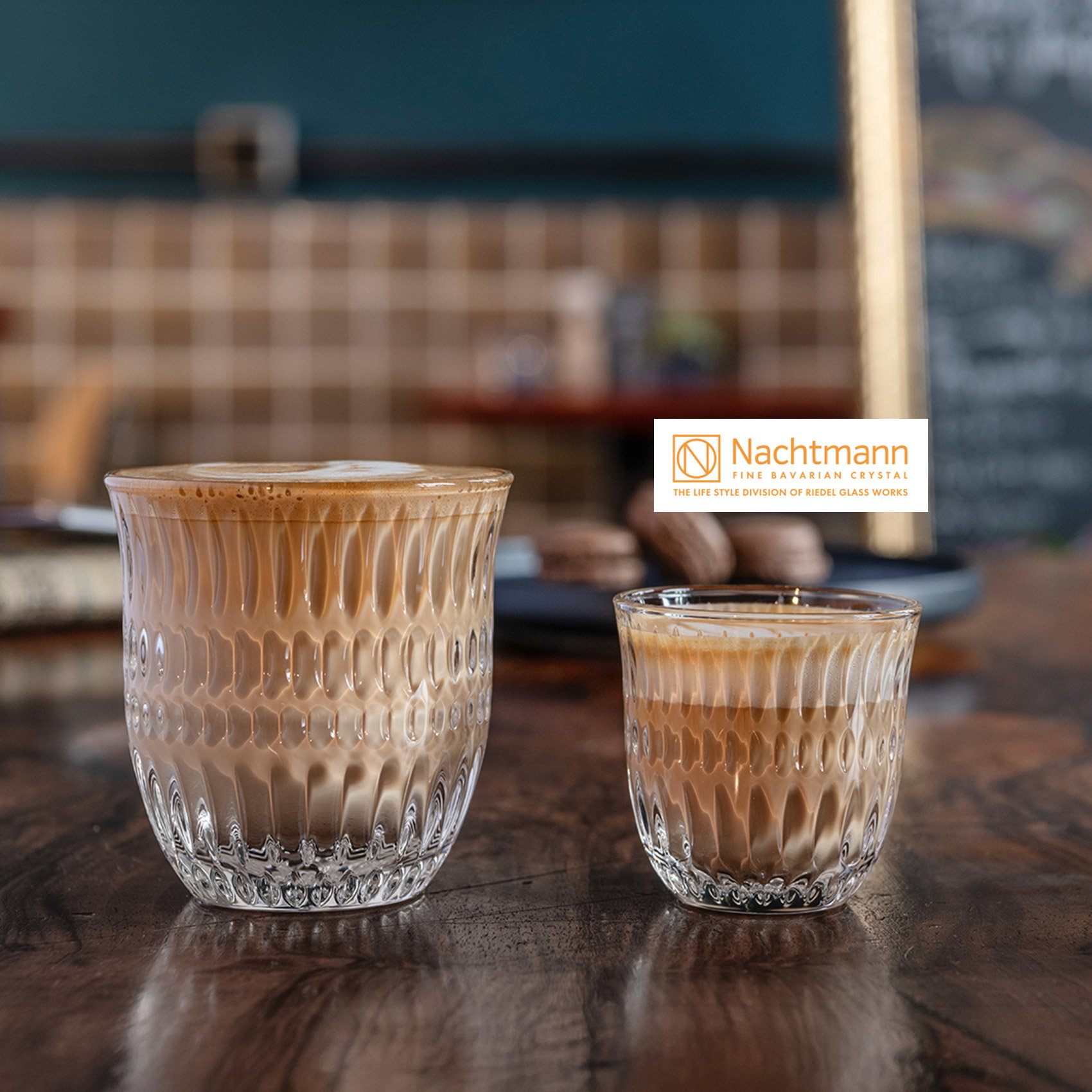 Zwei strukturierte Nachtmann Kristallgläser mit Latte Macchiato und Espresso auf Holztisch in stilvollem Café-Ambiente.