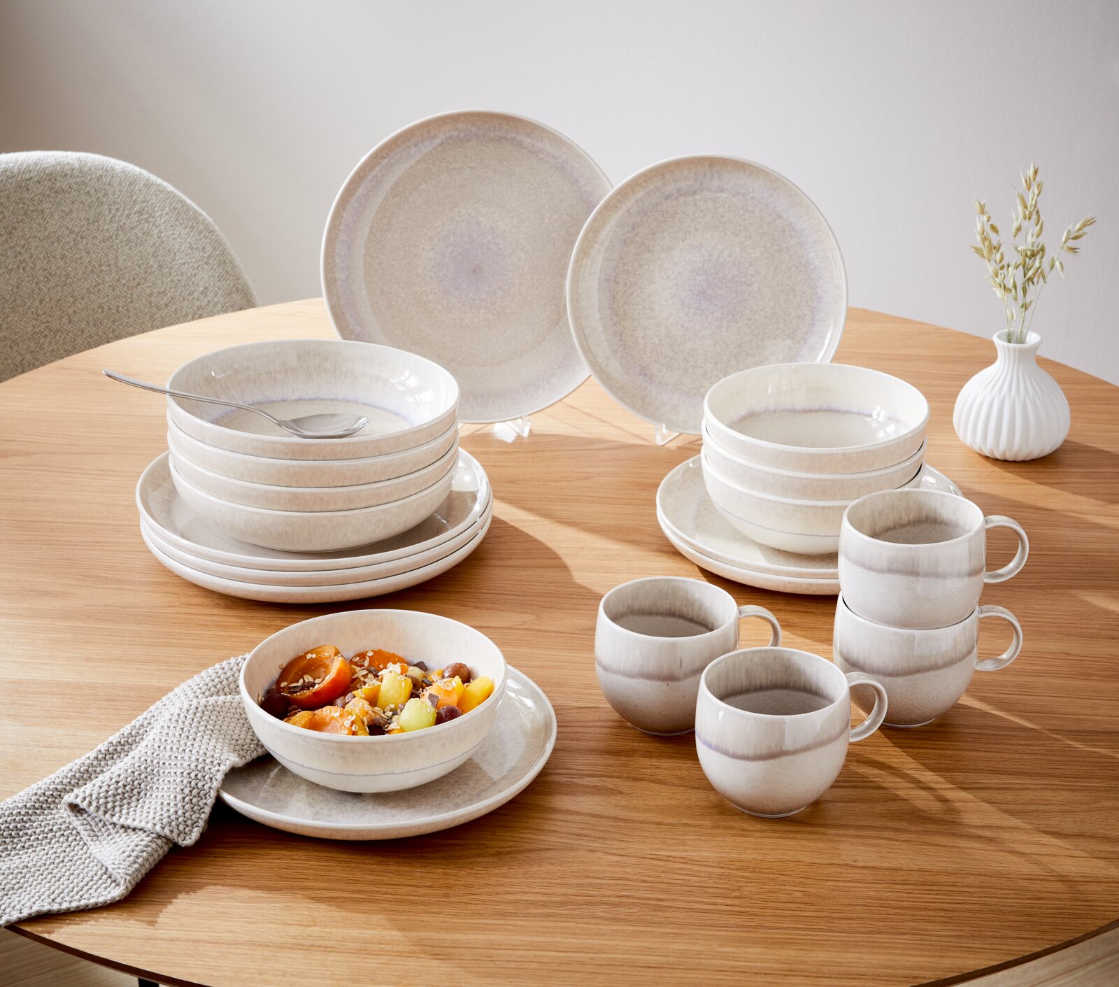 8-delig servies op een houten tafel, bestaande uit borden, schalen en kopjes in zachte beige- en grijstinten, zijaanzicht.