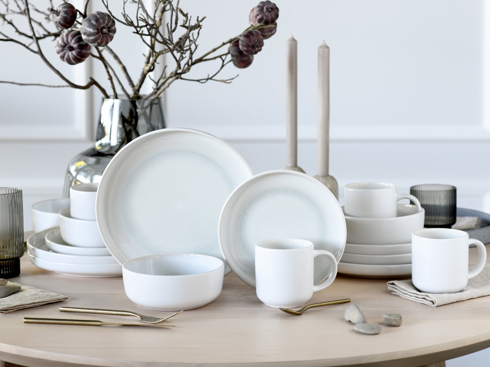 Elegantes 16-teiliges Kombiservice 'Ice' in Weiß mit dezentem Muster, präsentiert auf einem Tisch in einer stilvollen Tischdekoration mit Zweigen und Kerzen, aus frontaler Perspektive.