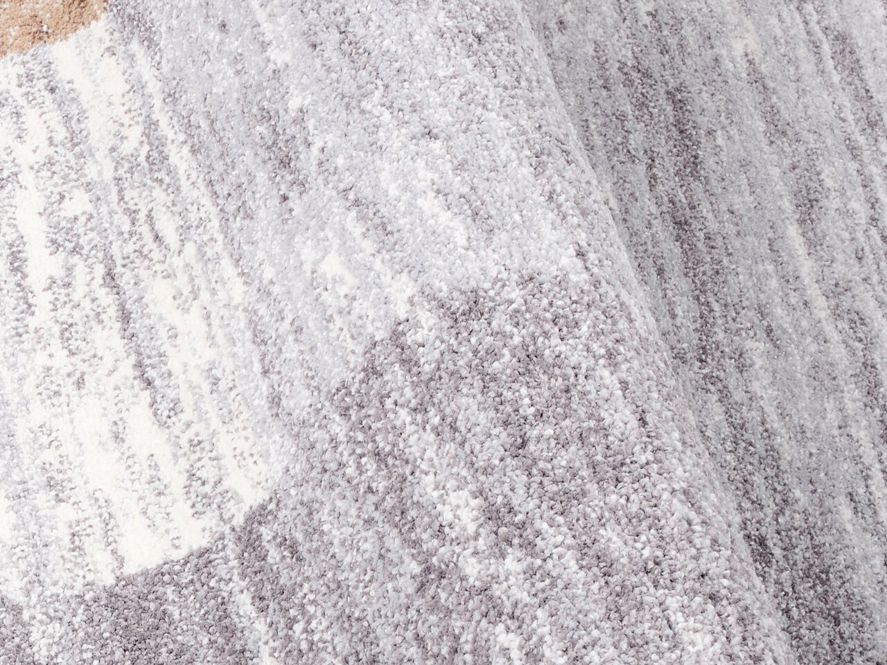 Nahaufnahme eines grauen und weißen Frisé-Teppichs mit weicher Textur, von der Seite betrachtet.