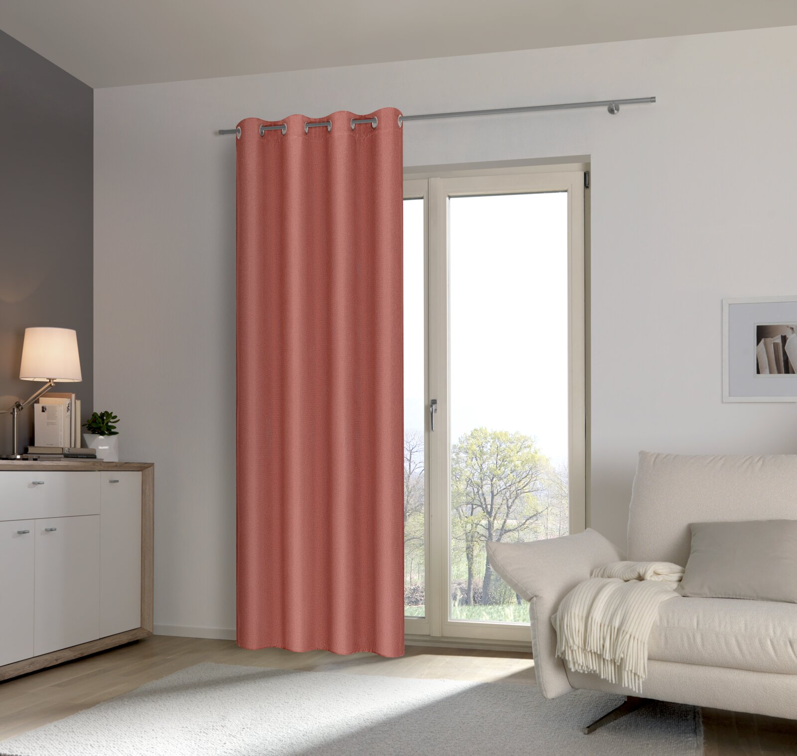 Rosa Ösenschal vor einem Fenster in einem modernen Wohnzimmer, seitliche Perspektive