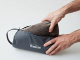Tempur Reisekissen in einer grauen Tasche, von zwei Händen gehalten, seitliche Perspektive