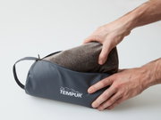 Tempur-reiskussen in een grijze tas, vastgehouden door twee handen, zijaanzicht