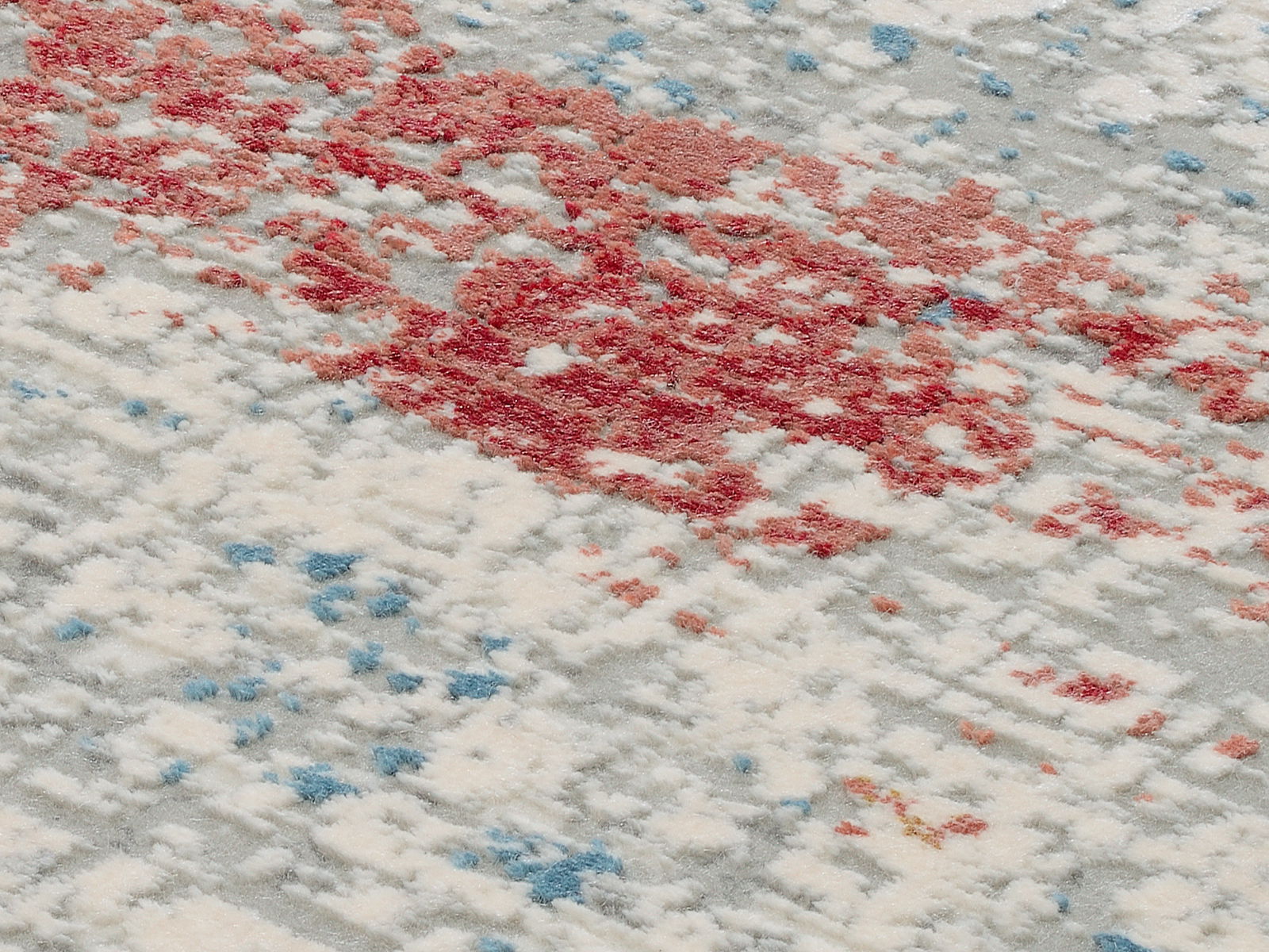 Nahaufnahme eines Designer-Teppichs mit abstraktem Muster in Rot, Blau und Weiß aus schräger Perspektive.
