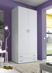 Weißer, zweitüriger Drehtürenschrank mit zwei Schubladen, in einem modernen Raum mit lila Wand und Blick aus dem Fenster.