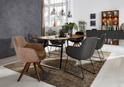 Esszimmer mit modernem Armlehnstuhl in Vorderansicht, umgeben von weiteren Stühlen und einem Holztisch, mit dekorativen Elementen im Hintergrund.