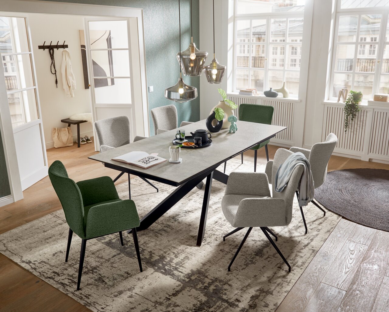 Moderner Esstisch mit grauer Tischplatte und schwarzen Beinen, umgeben von stilvollen Stühlen in einem hellen, eleganten Raum mit großen Fenstern. Perspektive von schräg oben.