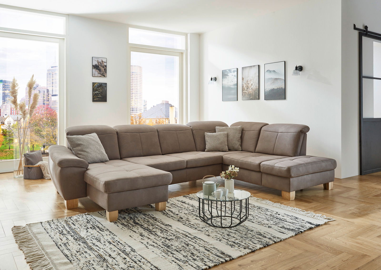 Große, moderne Polsterrundecke in einem hellen Wohnzimmer mit Blick auf die Stadt. Perspektive von vorne links.