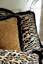 Nahaufnahme von Dekokissen mit verschiedenen Tiermustern, darunter Leoparden- und Zebramuster, in einer gemütlichen Wohnumgebung.
