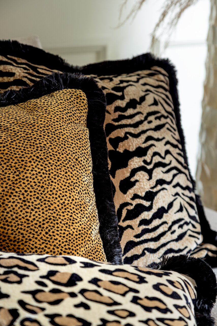 Close-up van sierkussens met verschillende dierenprints, waaronder luipaard- en zebraprint, in een gezellige woonkamer.