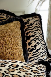 Close-up van sierkussens met verschillende dierenprints, waaronder luipaard- en zebraprint, in een gezellige woonkamer.