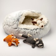 Weiches, flauschiges Tierbett in hellgrau mit einem Plüschspielzeug in Form eines Hundes darin. Zwei weitere Plüschtiere, ein orangefarbener und ein grauer Hund, liegen davor. Perspektive von schräg oben.