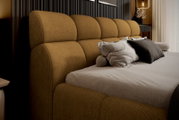 Seitliche Perspektive eines Polsterbettgestells mit beigem Kopfteil und Kissen in einem modernen Schlafzimmer.