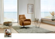 Cognackleurige relaxfauteuil met gestoffeerde armleuningen en een zwart draaivoetstel op een licht tapijt in een moderne woonkamer met uitzicht op zee; perspectief: vooraanzicht met een lichte zijaanzicht