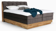 Boxspringbett mit braunem Stoffbezug und Holzrahmen, seitliche Perspektive