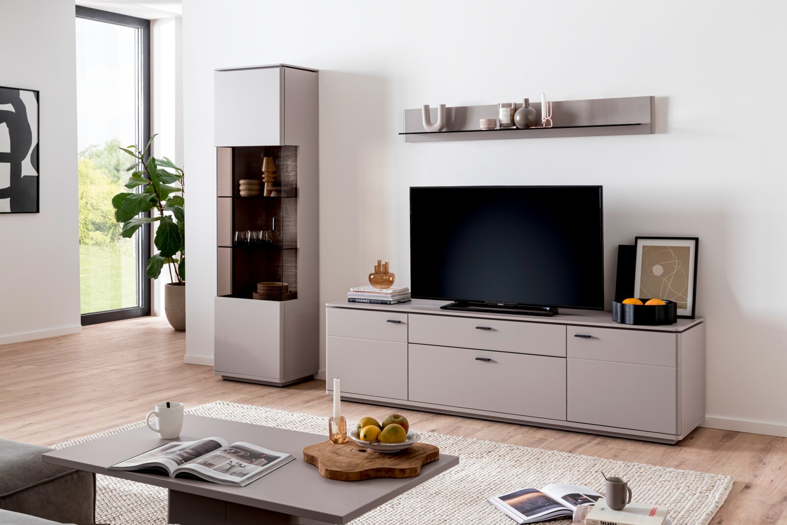 Zurbrüggen Wandkombination TORRENT Modernes Wohnzimmer mit grauem TV-Lowboard und Flachbildfernseher, passendem Wandregal sowie hoher Vitrine mit Glasfront; frontale Perspektive auf die Möbelwand.