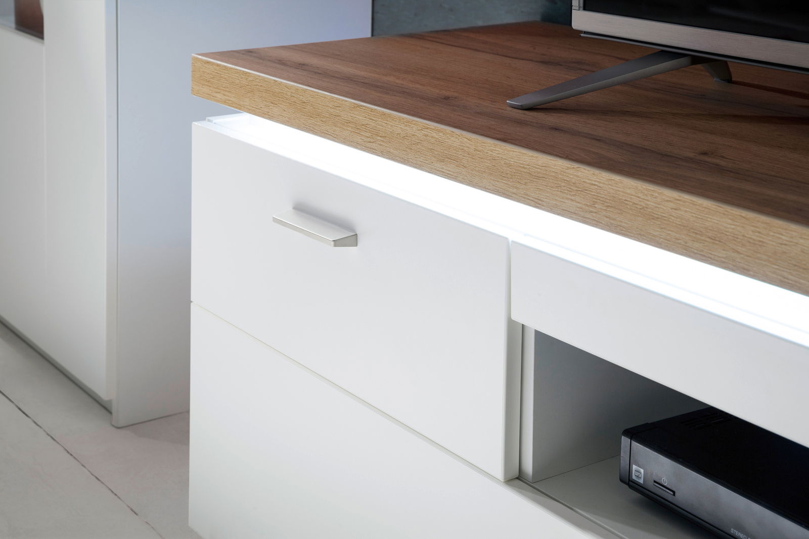 Nahaufnahme eines modernen TV-Elements mit weißer Front und Holzoberfläche, seitliche Perspektive.