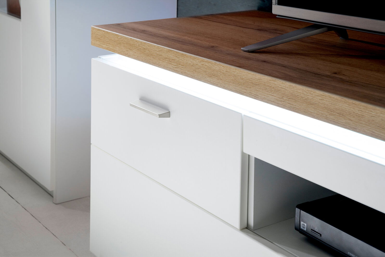 Nahaufnahme eines modernen TV-Elements mit weißer Front und Holzoberfläche, seitliche Perspektive.