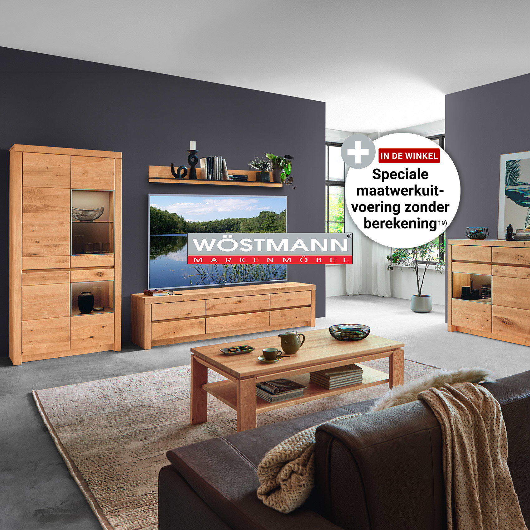 Modern ingerichte woonkamer met massieve eikenhouten meubels van Wöstmann, bestaande uit een vitrinekast, tv-lowboard, dressoir en salontafel tegen een donkergrijze wandafwerking.