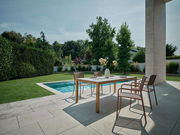 Moderner Stapelsessel auf einer Terrasse neben einem Tisch, mit Blick auf einen Pool und einen Garten im Hintergrund.