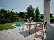Een moderne stapelstoel op een terras naast een tafel, met uitzicht op een zwembad en een tuin op de achtergrond.