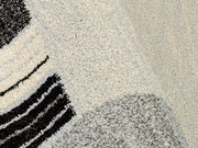 Nahaufnahme eines strukturierten Teppichs mit abstraktem Muster in Schwarz, Grau und Cremefarben, perspektivisch von oben fotografiert.