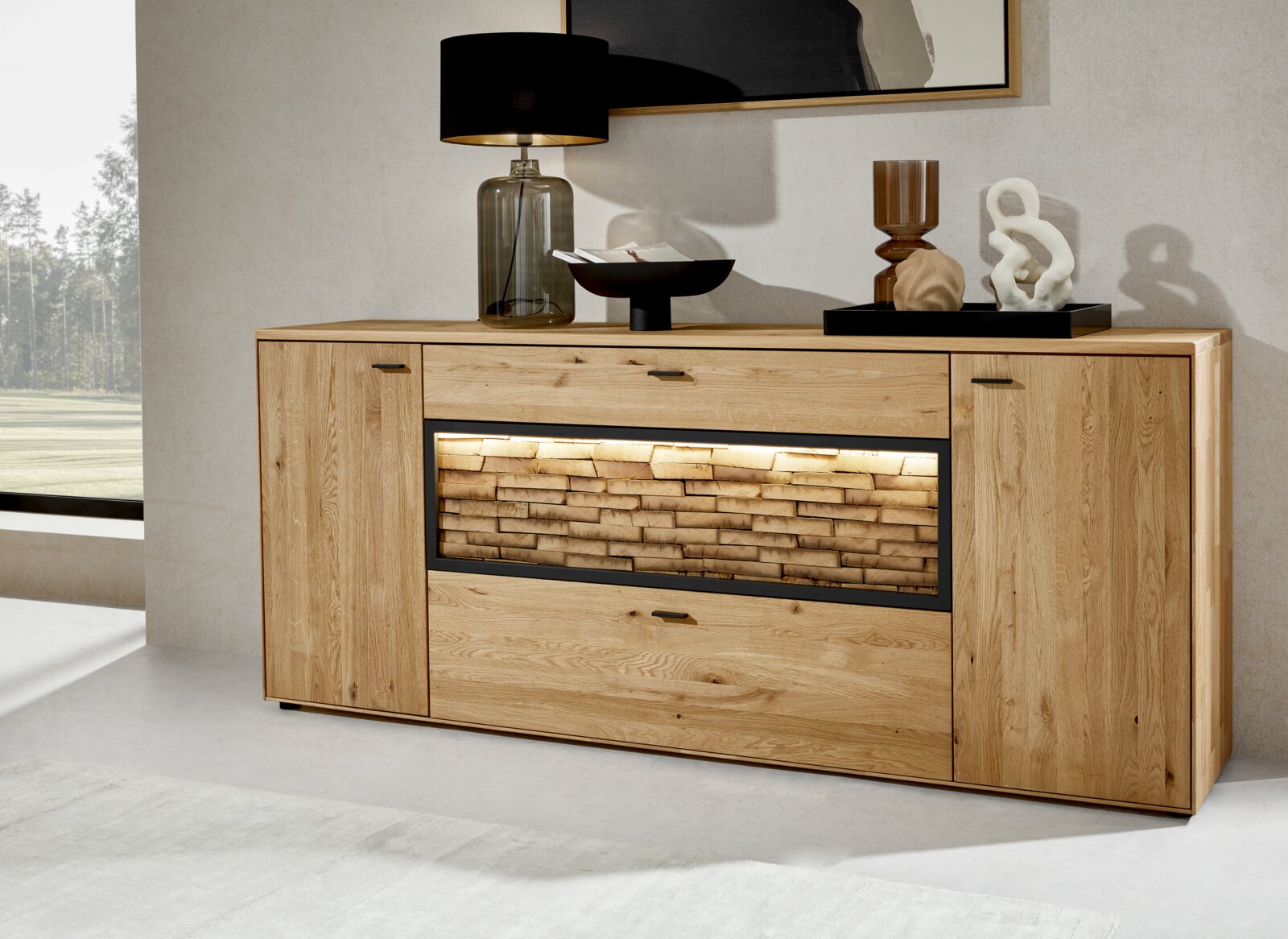 Valnatura Sideboard VALS Frontale Ansicht eines modernen Sideboards aus Holz mit dekorativer Steinoptik und Beleuchtung in der Mitte, dekoriert mit einer Lampe und Kunstobjekten.