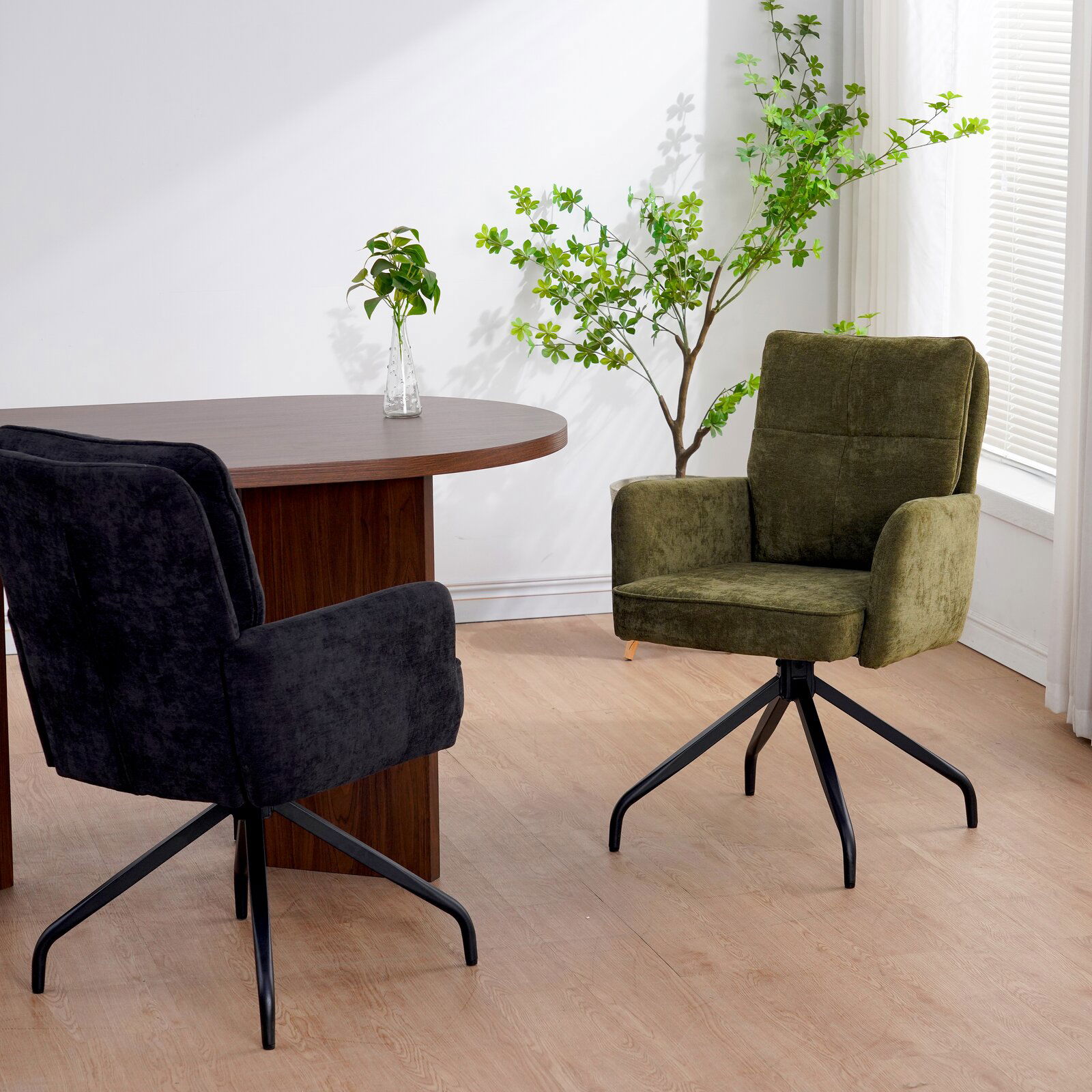 Zwei Schwingstühle in einem modernen Raum, einer in Schwarz und einer in Grün, mit einem runden Holztisch und Pflanzen im Hintergrund. Perspektive von der Seite.